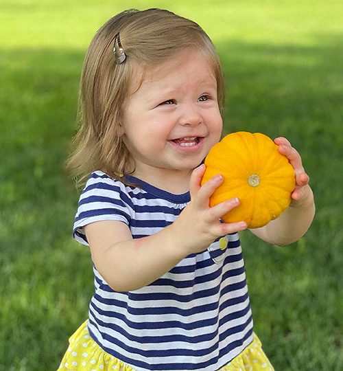 Happy toddler holding a mini pumpkin from the Pumpkin Patch at Prior Creek Farms